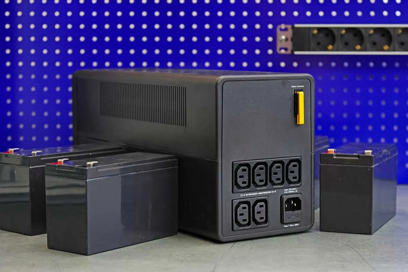 The back of a UPS unit showing its power outlets, with replacement batteries beside it